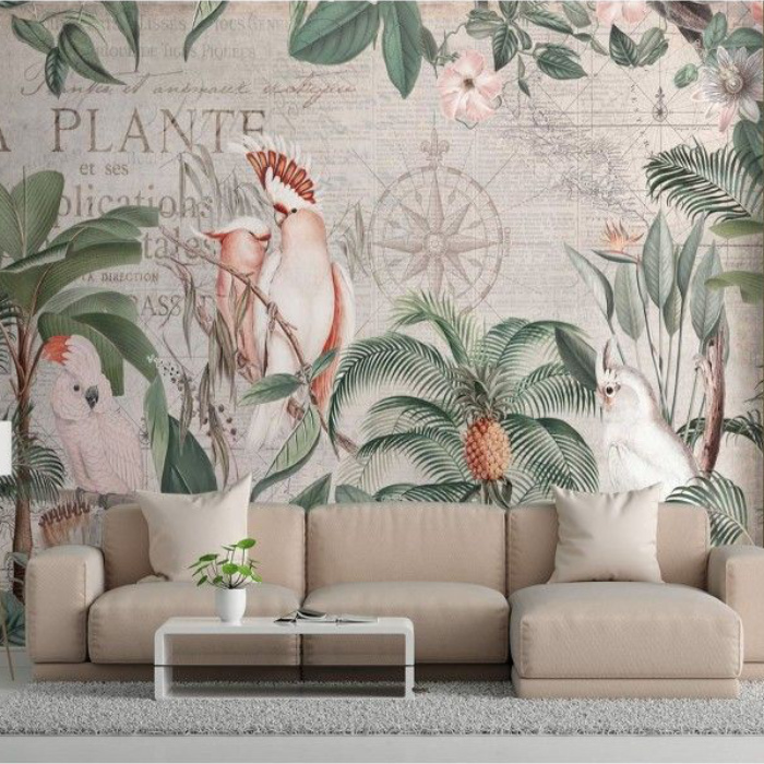 Tapeta z tropikalnym wzorem przedstawiającym papugi, liście palmowe i ananasa, na tle mapy świata, za beżową sofą z jasnymi poduszkami.